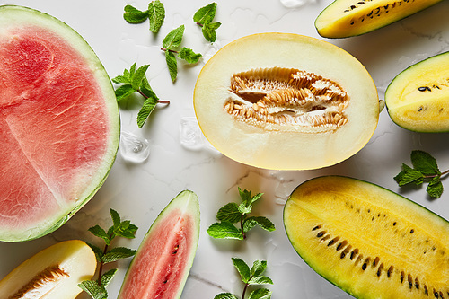 top view of cut delicious exotic yellow and red watermelons and melon on marble surface with mint and ice