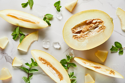 top view of cut delicious melon on marble surface with mint and ice