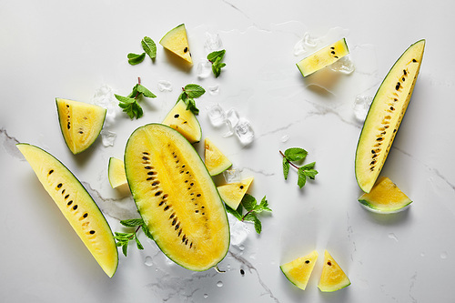 top view of cut delicious exotic yellow watermelon with ice and mint on marble surface