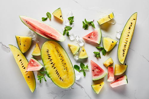 top view of cut delicious exotic yellow and red watermelons with ice and mint on marble surface