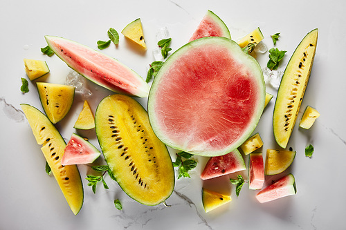 top view of delicious exotic yellow and red watermelons with ice and mint on marble surface