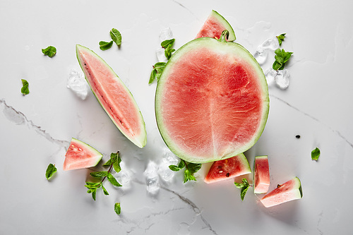 top view of cut delicious red watermelon with seeds on marble surface with ice and mint