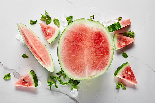 top view of cut delicious exotic red watermelon with seeds on marble surface with ice and mint