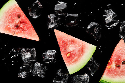 top view of red watermelon slices with melting ice isolated on black