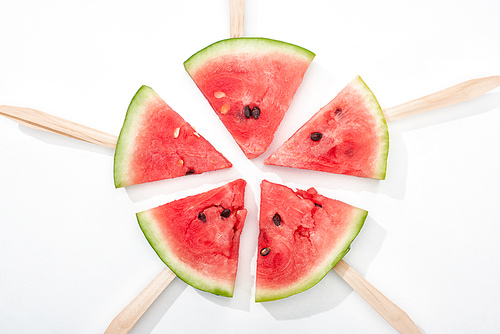 top view of delicious watermelon slices on wooden sticks on white background