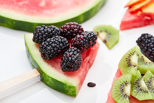 close up view of delicious dessert with watermelon on sticks, kiwi and blackberries on white background
