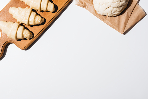 top view of fresh croissants on wooden cutting board near raw dough on white background