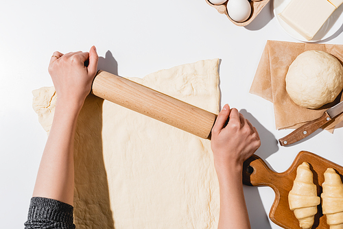 cropped view of woman rolling out dough for croissants on white background