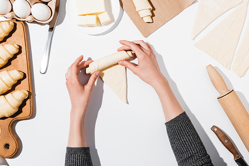 cropped view of woman rolling croissant on white background