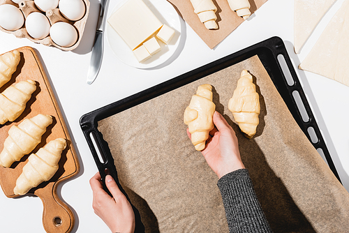 cropped view of woman putting croissants on baking tray on white background
