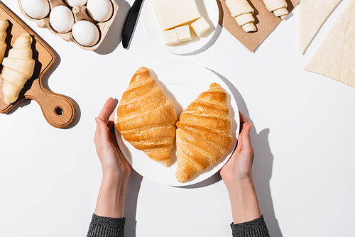 cropped view of woman holding plate with baked croissants on white background