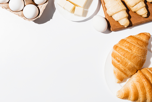 top view of fresh raw and baked croissants near butter and eggs on white background