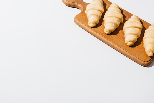 fresh raw croissants on wooden cutting board on white background