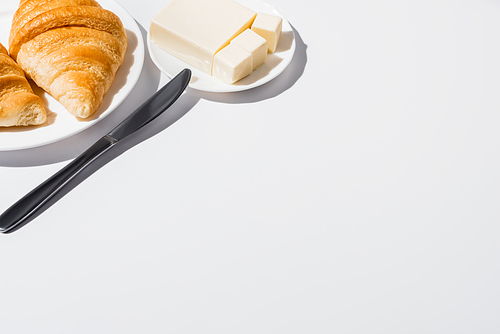 tasty fresh baked croissants on plate near butter with knife on white background