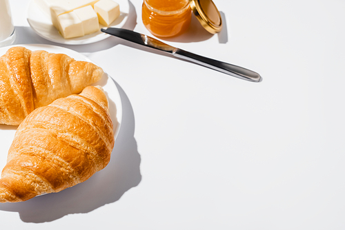 tasty fresh baked croissants on plate near butter with knife and jam on white background
