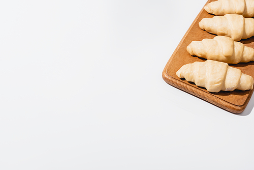 fresh raw croissants on wooden cutting board on white background