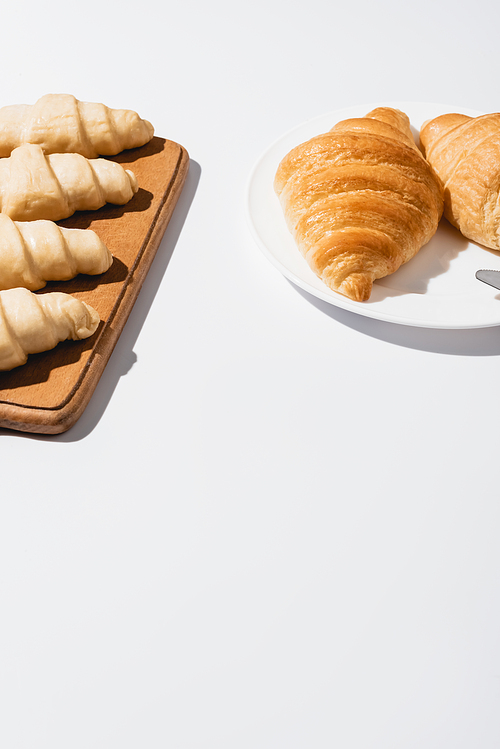 fresh baked and raw croissants on white background