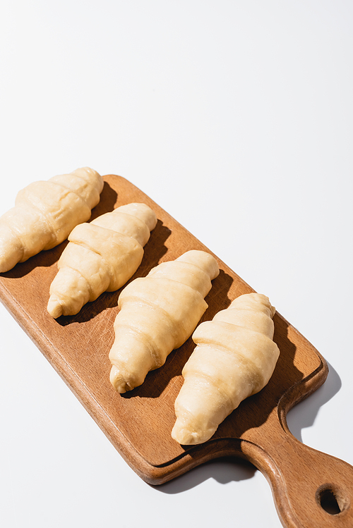 raw fresh croissants on wooden cutting board on white background