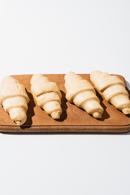 raw fresh croissants on wooden cutting board on white background