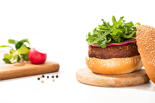 selective focus of delicious vegan burger with radish and arugula on wooden board near black pepper on white background
