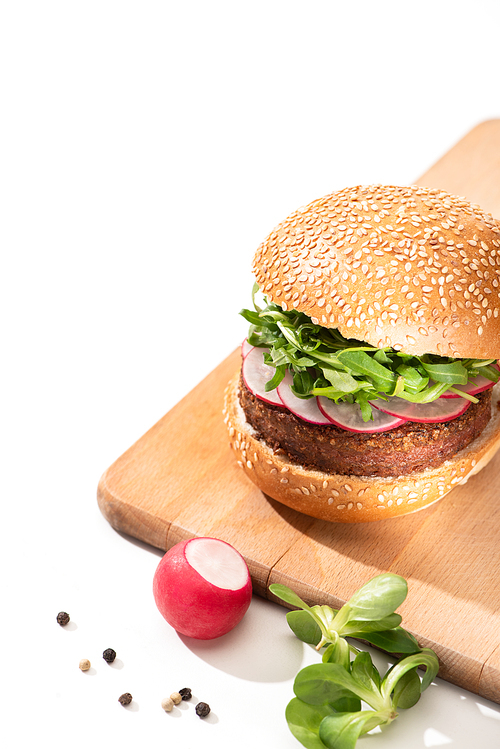 delicious vegan burger with radish and arugula on wooden board with black pepper on white background