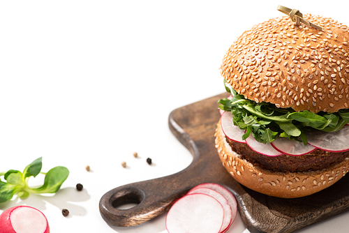 selective focus of  delicious vegan burger with radish and arugula on wooden board with black pepper on white background