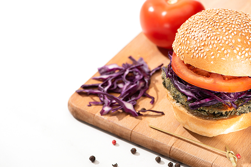 delicious vegan burger with red cabbage and tomato on wooden board with black pepper on white background