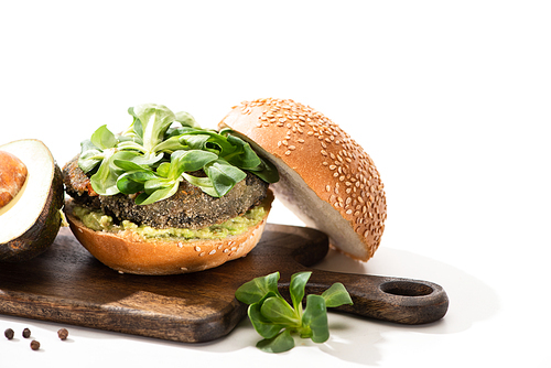 delicious green vegan burger with microgreens, avocado, black pepper on wooden cutting board on white background