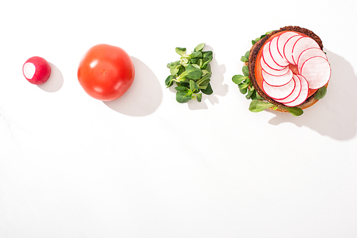 top view of vegan burger with radish, tomato and sprouts on white background