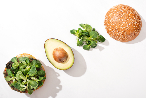 top view of vegan burger with avocado and microgreens on white background