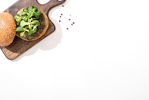 top view of vegan burger with microgreens on wooden board on white background