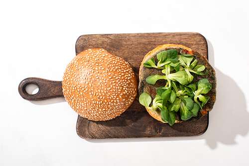 top view of vegan burger with microgreens on wooden cutting board on white background
