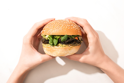 cropped view of woman holding delicious vegan burger on white background