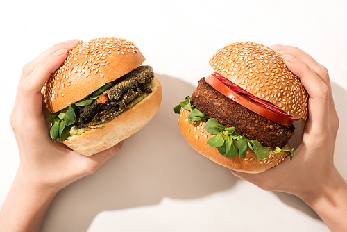 cropped view of woman holding delicious vegan burgers on white background