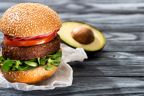 selective focus of tasty vegan burger with radish served on wooden table with avocado half