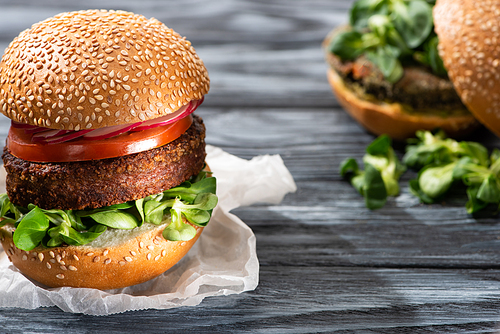 selective focus of tasty vegan burgers with microgreens and vegetables served on wooden table