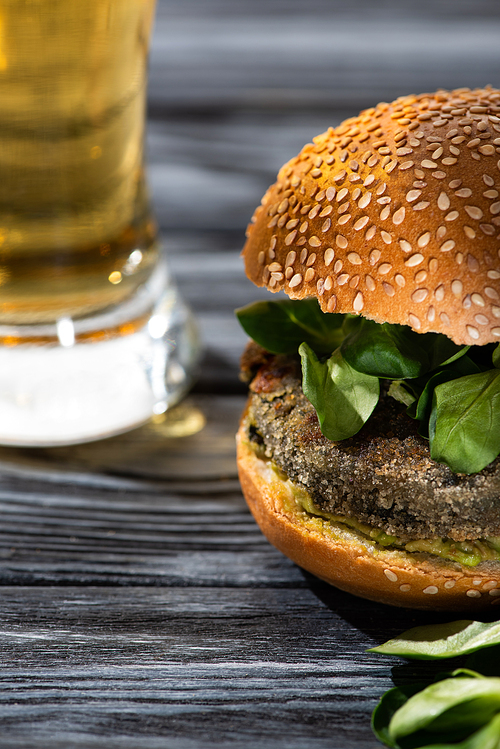 selective focus of tasty vegan burger with microgreens served on wooden table with glass of beer