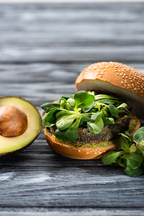 tasty vegan burger with microgreens served on wooden table with avocado half