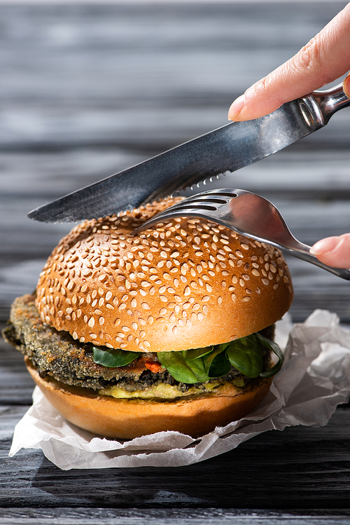 cropped view of woman cutting tasty vegan burger with fork and knife