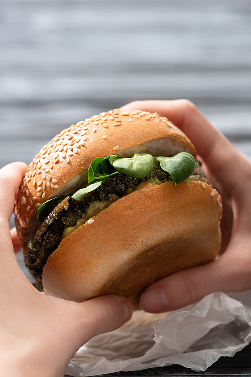 cropped view of woman holding tasty vegan burger with microgreens