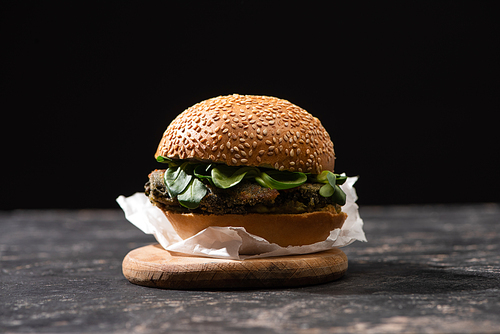 tasty vegan burger with microgreens served on wooden board isolated on black