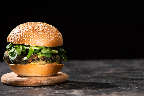 tasty vegan burger with microgreens served on wooden board isolated on black