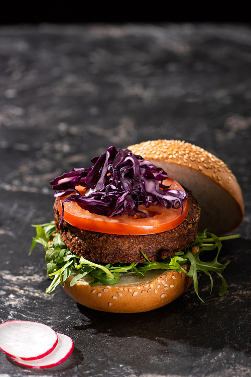 tasty vegan burger with tomato, red cabbage and greens served on textured surface with radish