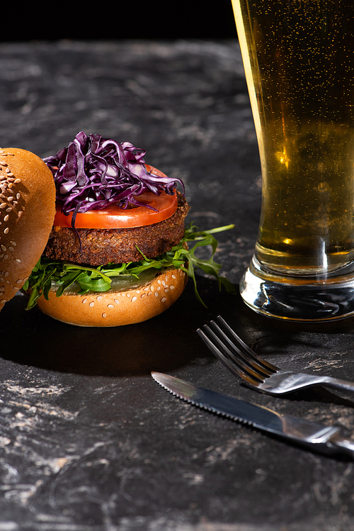 tasty vegan burger with tomato, red cabbage and greens served on textured surface with beer and cutlery