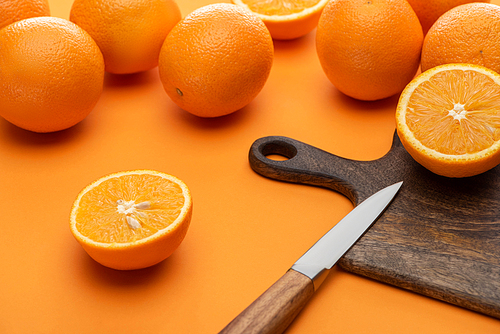 fresh juicy whole and cut oranges on cutting board with knife on colorful background