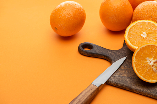 fresh juicy whole and cut oranges on cutting board with knife on colorful background