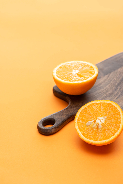 ripe juicy orange halves on wooden cutting board on colorful background