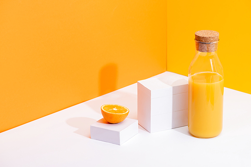 fresh orange juice in glass bottle near ripe orange on white surface on orange background