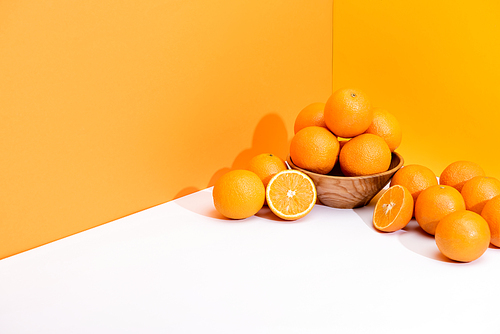 fresh ripe oranges in bowl on white surface on orange background
