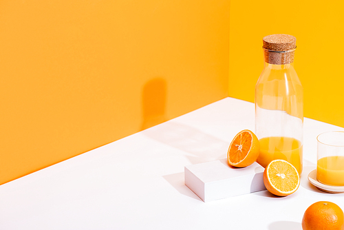 fresh orange juice in glass and bottle near ripe oranges on white surface on orange background